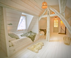 A loft bedroom with a sloped ceiling, a bed, a window, a small stool, a basket, and a staircase. - New Listing (Saint-Philbert-des-Champs)