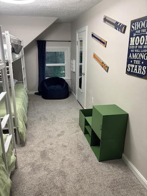 A child's bedroom with bunk beds, a bean bag chair, a green storage box, and motivational wall art.