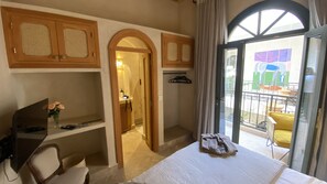 Ein Hotelzimmer mit Bett, Schreibtisch mit Computer, Stuhl, kleinem Tisch und Blumenvase, sowie Blick auf den Balkon.