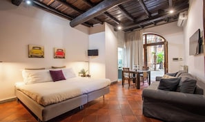 Quarto com cama, sofá, mesa de jantar com cadeiras e televisão na parede.