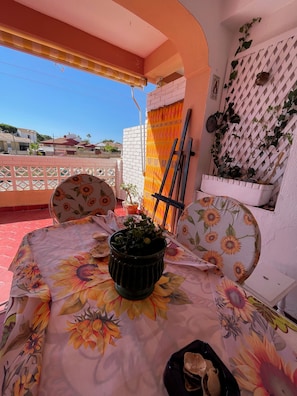 Un patio con una mesa cubierta por un mantel floral, una planta en maceta y una silla.