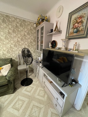 Een woonkamer met een bank, een televisie, een kast en een ventilator.