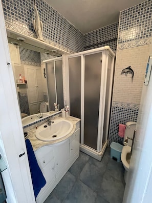Un baño con lavamanos blanco, espejo y cabina de ducha.