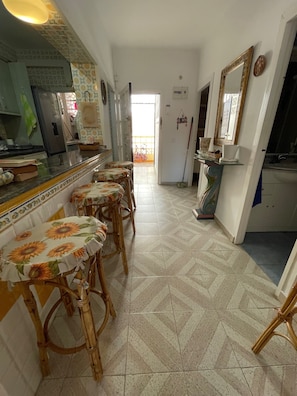 Una cocina con comedor, que incluye una encimera larga con taburetes, un refrigerador y piso de baldosas.
