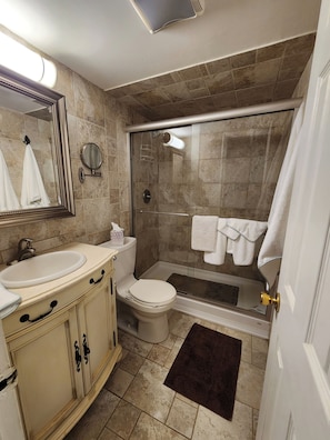 Ein Badezimmer mit Toilette, Waschbecken, Spiegel und Duschbereich.
