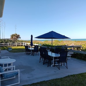 Eine Terrasse im Freien mit Tischen und Stühlen, einem Holzzaun und Blick aufs Meer.