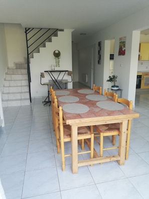 A dining area with a wooden table and chairs, a staircase, and a kitchen in the background. - New Listing (Arbus)