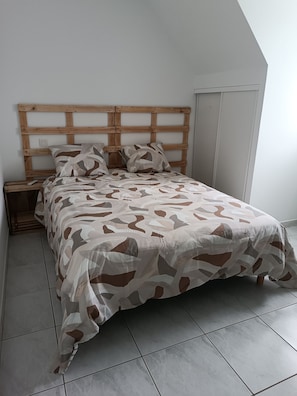 A bed with a patterned bedspread, a wooden headboard, a nightstand, and a tiled floor. - New Listing (Arbus)