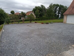 A gravel driveway leading to a house with a red roof, surrounded by greenery and a fence. - New Listing (Arbus)