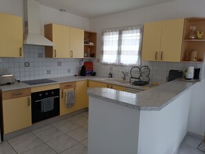 A kitchen with a central island, a built-in oven, and a window with curtains. - New Listing (Arbus)