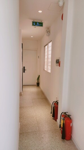 A hallway with a fire extinguisher mounted on the wall, a potted plant, and a door at the end. - D1 Heart · Rooftop•Kitchen•Lift · Cotta @ Cozinema (Thành phố Hồ Chí Minh)