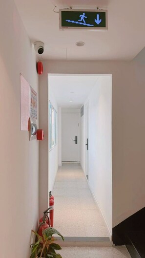 A corridor with a fire exit sign, a fire extinguisher, and a security camera. - D1 Heart · Rooftop•Kitchen•Lift · Cotta @ Cozinema (Thành phố Hồ Chí Minh)
