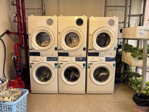 A laundry area with multiple stacked washing machines, a red pipe, and a blue laundry basket. - D1 Heart · Rooftop•Kitchen•Lift · Cotta @ Cozinema (Thành phố Hồ Chí Minh)