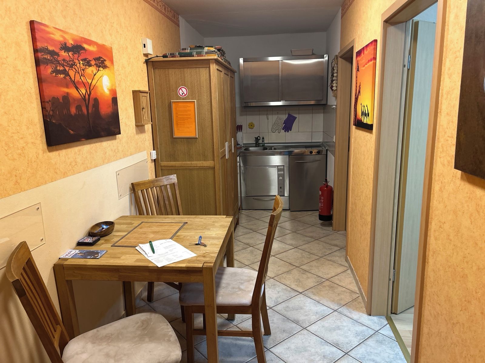 A compact kitchen with modern appliances, a dining area with a wooden table and chairs, and artwork on the walls.