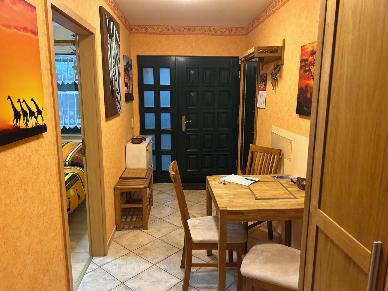 Un'area pranzo con un tavolo e sedie in legno, una porta nera e opere d'arte alle pareti.