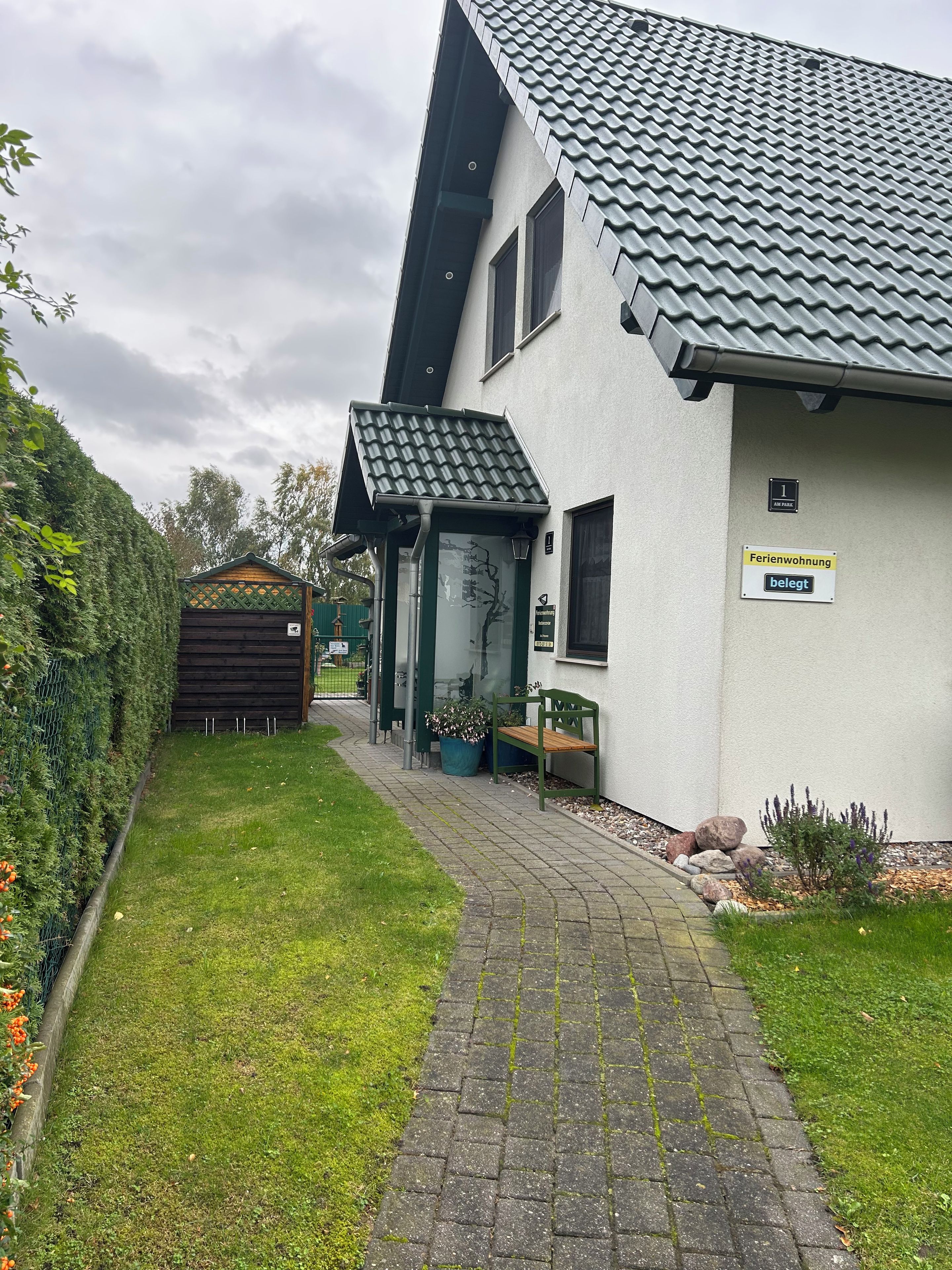 A residential building with a paved driveway, a covered entrance, and a sign indicating it is a 'Ferienwohnung' (holiday home).