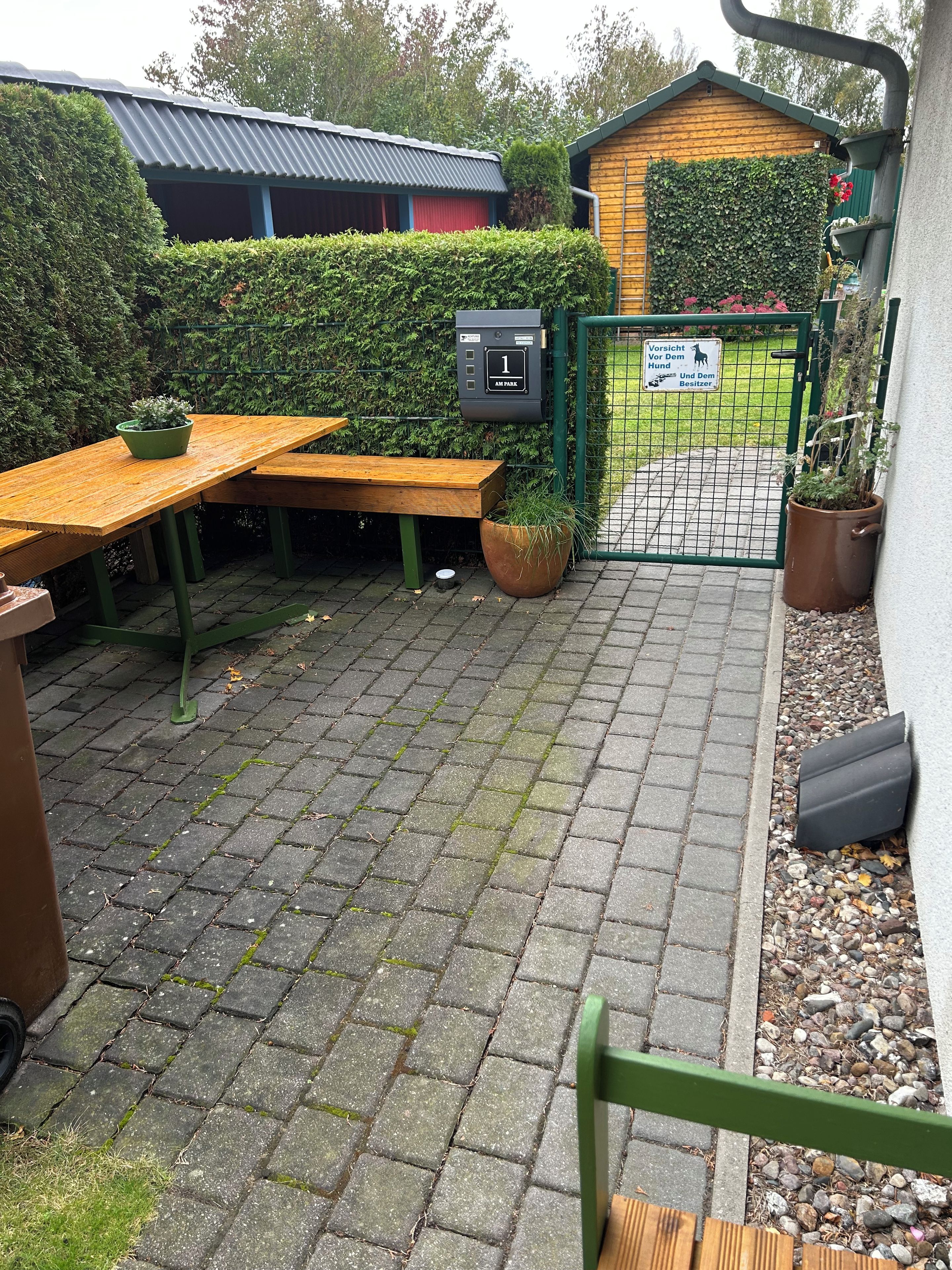 A paved outdoor area with a wooden bench, a potted plant, and a metal gate.