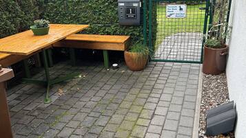 A paved outdoor area with a wooden bench, a potted plant, and a metal gate.