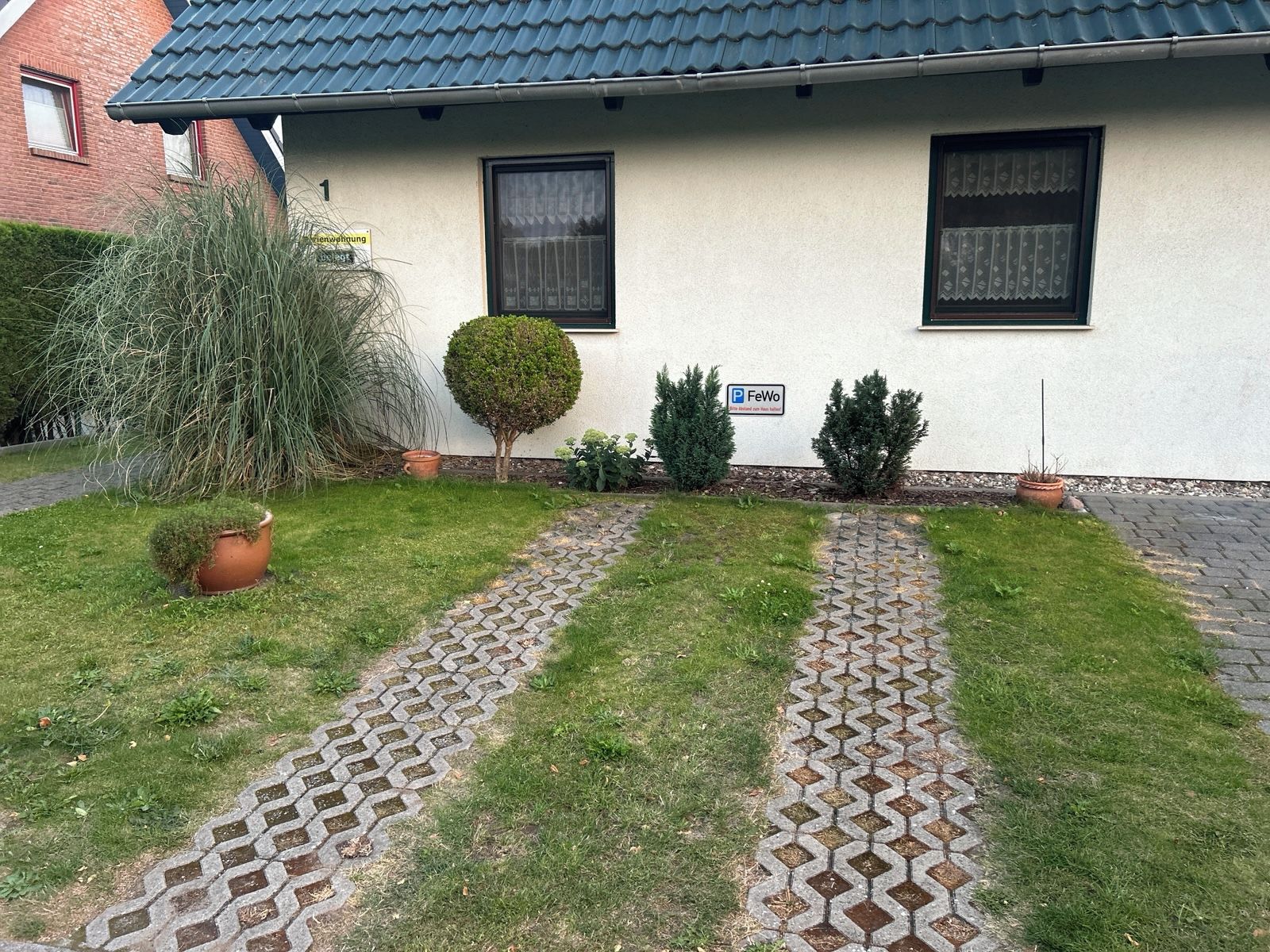 A house with a paved driveway, a small garden with a tree, and a sign indicating parking availability.