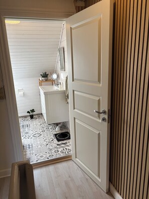 Ein Durchgang zu einem Badezimmer mit einem weißen Waschbecken, einem Spiegel und einer Topfpflanze.