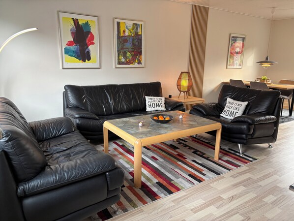 Ein modernes Wohnzimmer mit einem schwarzen Ledersofa, einem Holztisch und einem Streifen Teppich.
