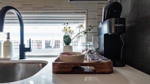 Une cuisine équipée d’un robinet moderne, d’une machine à café Keurig, d’un distributeur de liquide vaisselle, d’un vase orné d’orchidées et d’un plateau contenant des capsules de café.