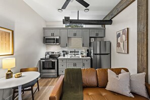 Une cuisine compacte dotée d’appareils électroménagers modernes, un coin repas avec une table et des chaises, et un espace salon confortable avec un canapé et des coussins.
