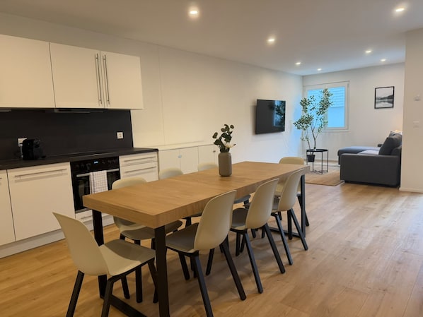 Een moderne keuken met witte kasten, een zwart aanrecht en een eethoek met een houten tafel en stoelen.