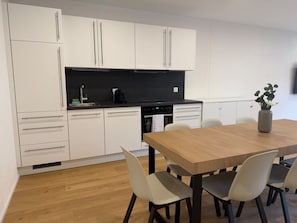 Una cocina moderna con armarios blancos, encimera negra y una mesa de comedor de madera con sillas.