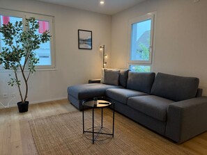 Una sala moderna con un sofá seccional gris, una mesita redonda y dos plantas en macetas.