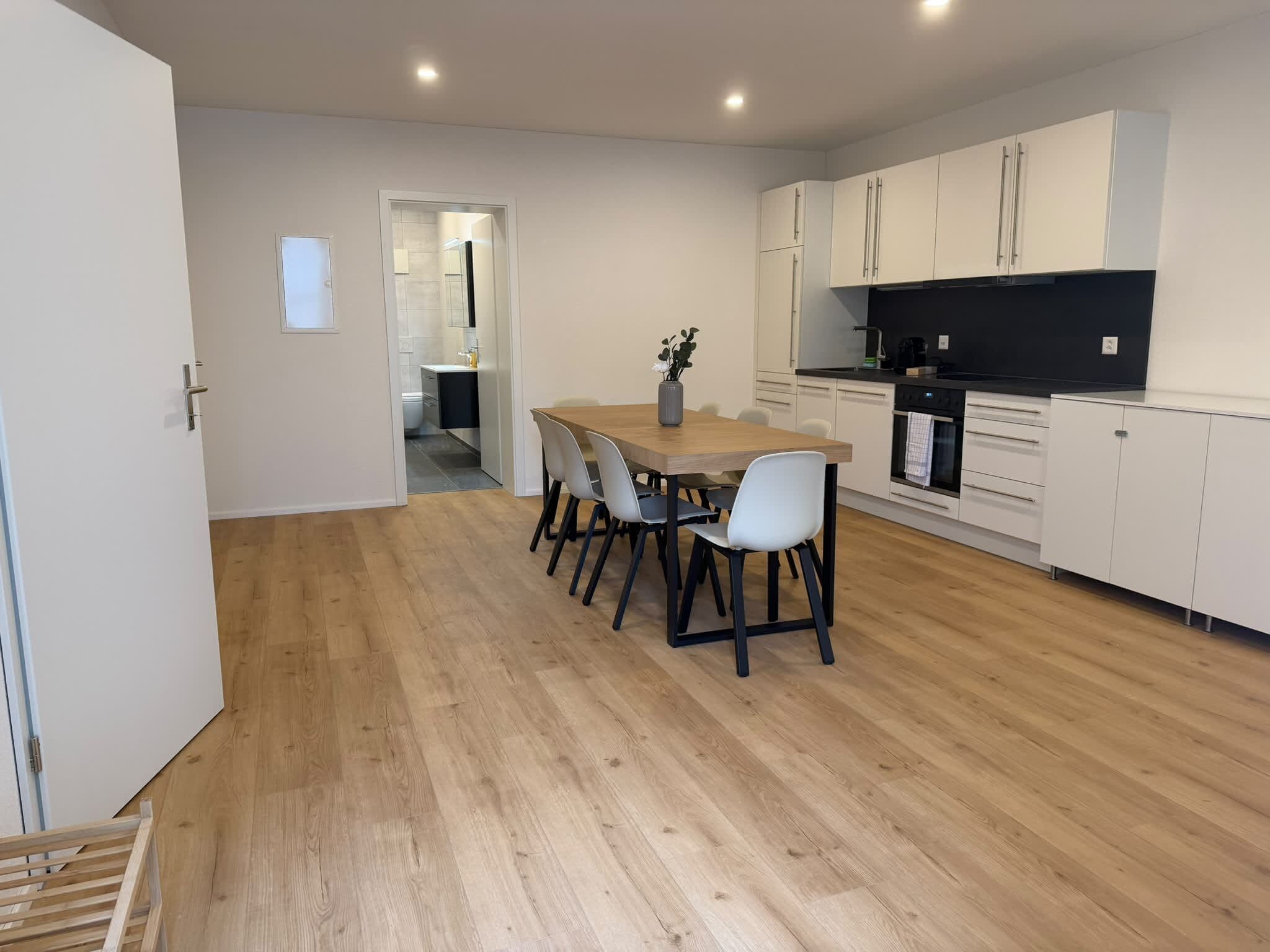 Een moderne keuken met witte kasten, een houten eettafel en een zwart aanrecht.