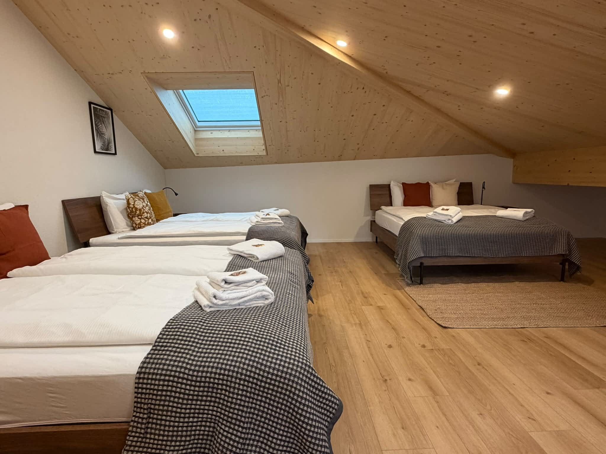 Een kamer met drie op een rij staande bedden, een dakraam en houten vloeren.