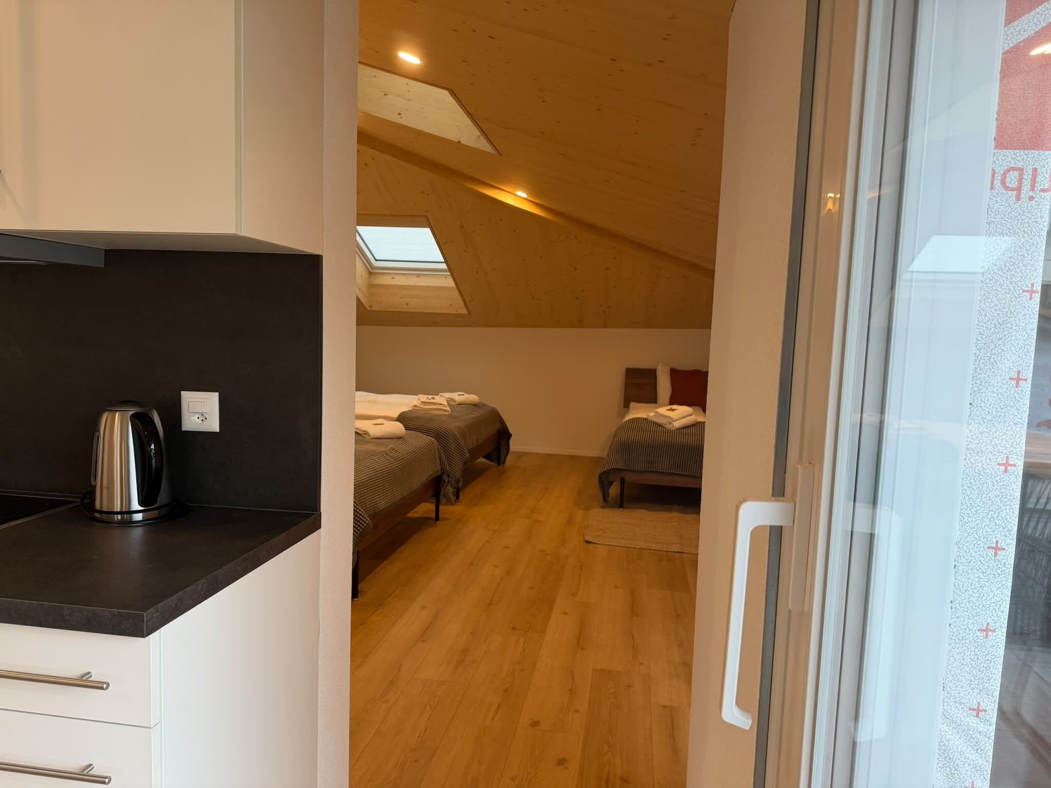 Een kleine kamer met een kitchenette, een bed en een dakraam.