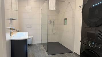 Une salle de bain moderne avec une douche à parois de verre, des toilettes, un lavabo et un lave-linge noir.