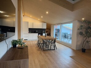 Una cucina moderna con mobili bianchi, un'area pranzo con tavolo e sedie in legno, e un'ampia finestra con vista sull'esterno.