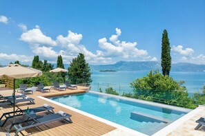 Ein Poolbereich mit Liegestühlen und Sonnenschirmen, mit Blick auf ein Gewässer und ferne Berge.