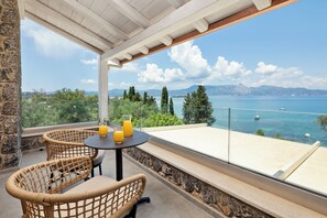 Ein Balkon mit Korbstühlen und einem Tisch, mit Blick auf ein Gewässer mit Booten und Bergen im Hintergrund.
