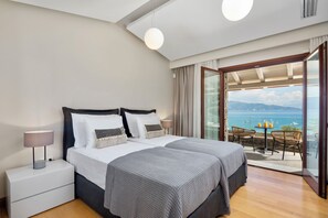 Ein Schlafzimmer mit Bett, Nachttischen und Meerblick durch eine Glastür.