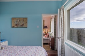 A bedroom with a bed, a painting, and a view through an open door to a living area. - Delightful Cottage, Strangford Lough, County Down (Newtownards)