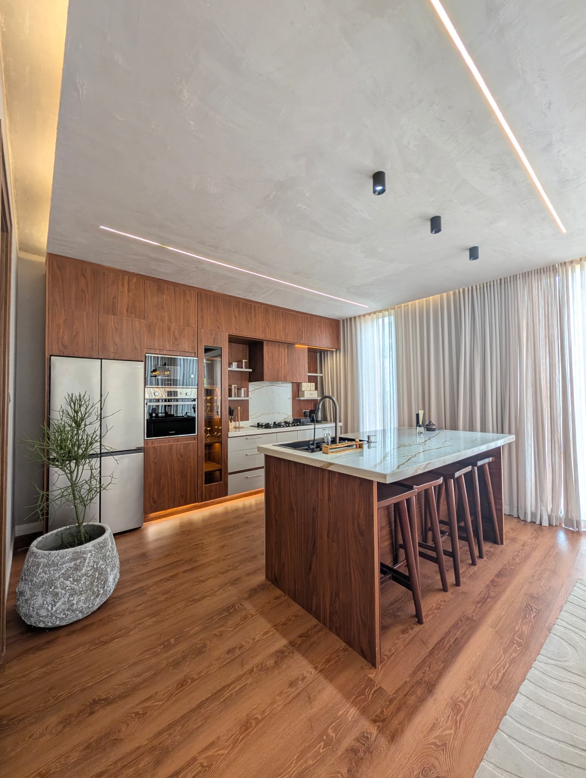 Eine moderne Küche mit Holzschränken, einer zentralen Kochinsel mit Barhocker und einem eingebauten Ofen.