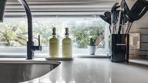 Une cuisine équipée d’un évier, de deux bouteilles de liquide vaisselle, d’une plante en pot et d’ustensiles de cuisine.