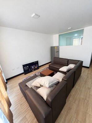 A modern living room with a sectional sofa, a flat-screen TV, and a refrigerator. - Refugio Quiteño (Quito)