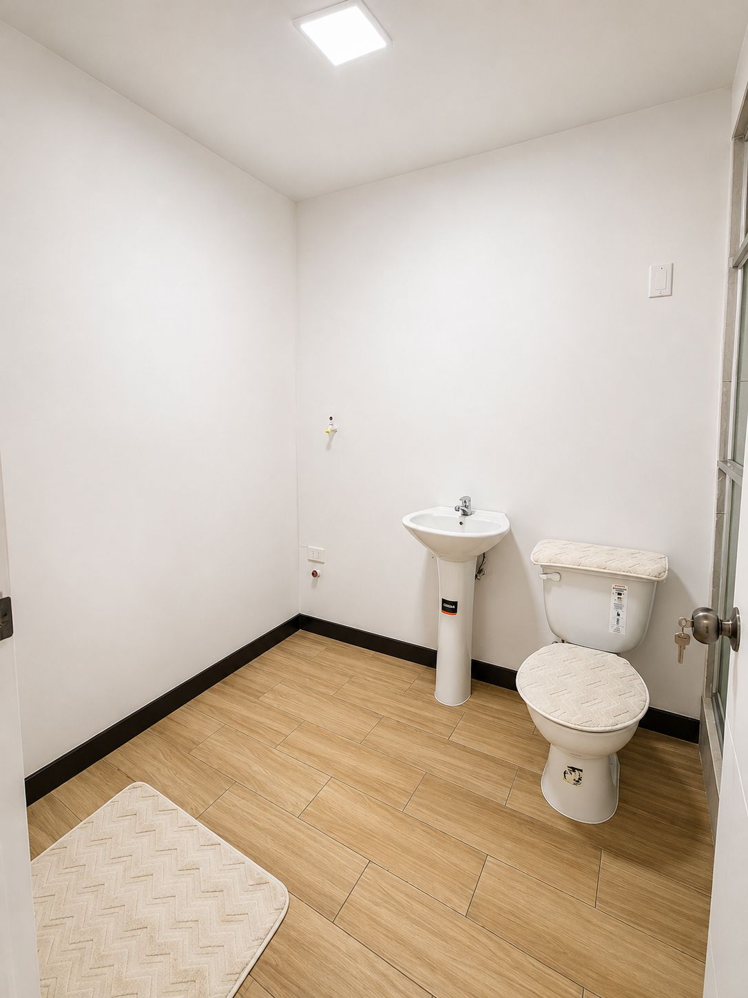 A small, clean bathroom with a toilet, sink, and a wooden floor.