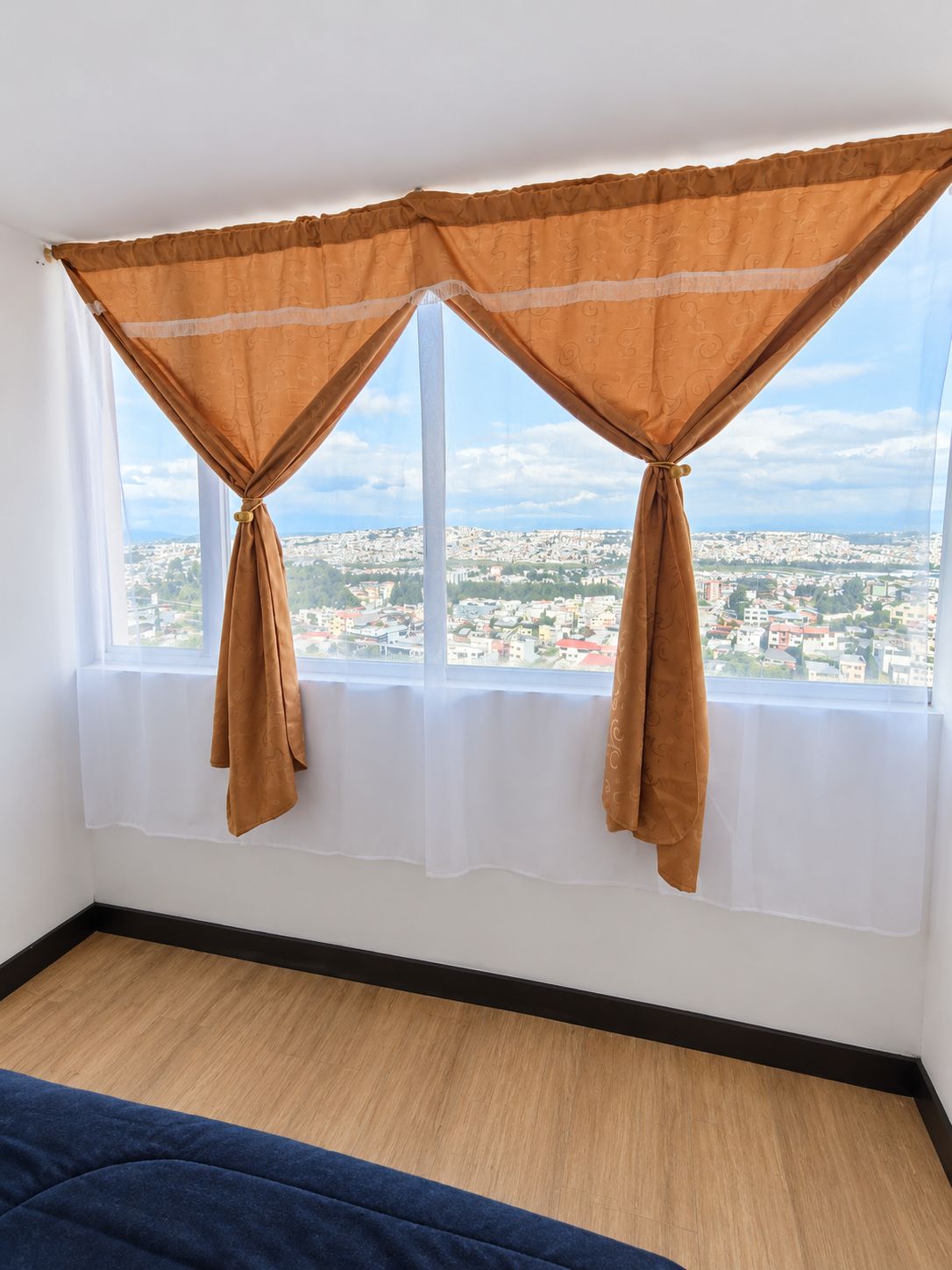 A room with a large window, curtains, a wooden floor, and a blue sofa.