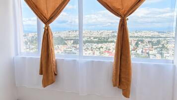 A room with a large window, curtains, a wooden floor, and a blue sofa.