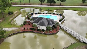A house with a swimming pool surrounded by water, a bridge, and a golf course in the background. - Two bedroom condo overlooking fairways of Calabash golf course. (Calabash)