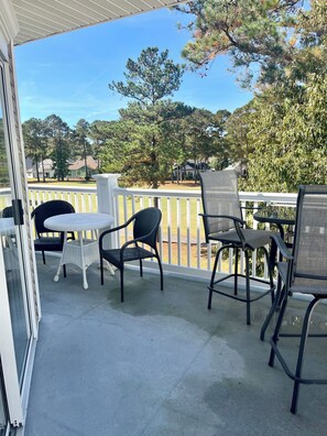 A covered outdoor area with a table and chairs, a white railing, and a view of houses and trees. - Two bedroom condo overlooking fairways of Calabash golf course. (Calabash)