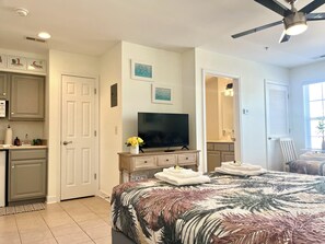 A bedroom with a bed, a television, a ceiling fan, and a bathroom visible through an open door. - Two bedroom condo overlooking fairways of Calabash golf course. (Calabash)