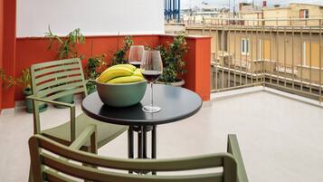 Een balkon met een tafel, stoelen, een schaal bananen en twee wijnglazen.