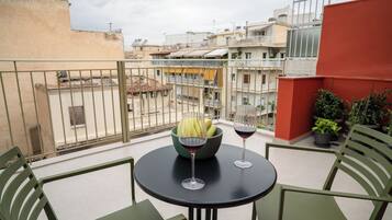 Een balkon met een tafel, stoelen, een schaal fruit en twee wijnglazen.